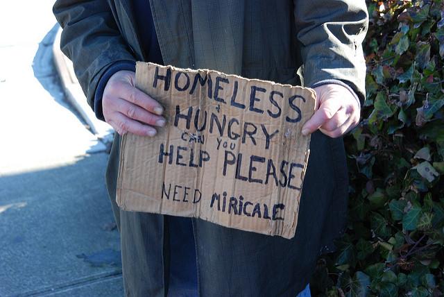homeless person holding a sign asking for help